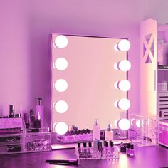 a vanity mirror with lights on it in front of a purple wall and counter top