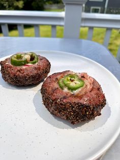 two meat patties on a white plate with green peppers