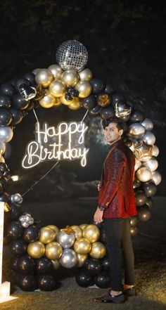 a man standing in front of a happy birthday sign surrounded by balloons and disco balls