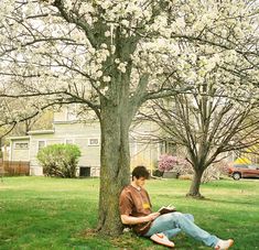 a man sitting under a tree reading a book