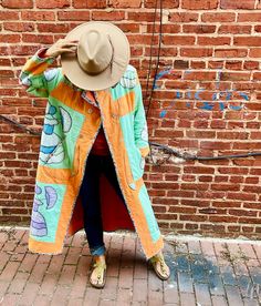 a woman standing in front of a brick wall with a hat on her head and coat over her shoulders