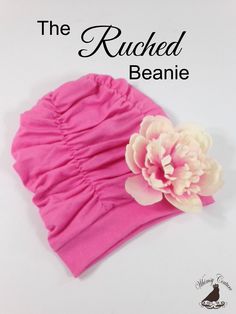 the ruched beanie is pink with a flower on it and text overlay reads,