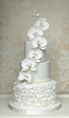 a three tiered cake with white flowers and pearls on the bottom is displayed against a floral wallpaper