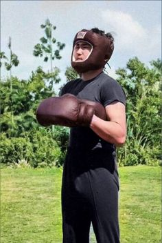 a man wearing a football helmet and holding a ball in one hand while standing on a field with trees in the background