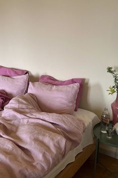 a bed with pink sheets and pillows on top of it next to a small table