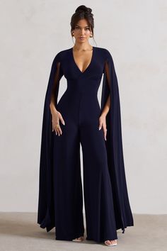 One of our favourite statement jumpsuits of the season. Emmanuela is an elegant ensemble for any formal event. Boasting a sculpting plunge neckline. what defines this flattering navy piece is floor sweeping cape sleeves and a contemporary cut-out back detail. For the perfect graduation look. team yours with some court shoes like Blade. Features - Premium stretch jersey- Plunge neckline - Cape sleeves- Button closure - Back cut out- Wide leg Sizing & Fit Model is 5'8 and wears UK size 8 / US size Jumpsuit With Cape, Cape Jumpsuit, Graduation Look, Midi Bridesmaid Dress, Casual Fridays, Black Tie Gala, Party Dress Long Sleeve, Cape Sleeves, Black Sequin Dress