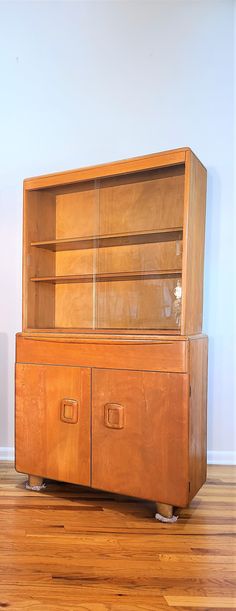 an old wooden cabinet with glass doors on the front and bottom shelves, sitting on top of a hard wood floor