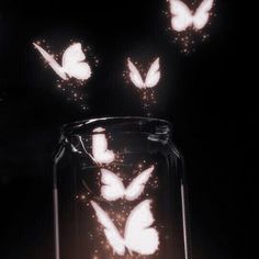 some butterflies are flying out of a jar in the dark with light coming from it