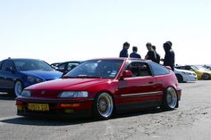 several cars parked in a parking lot with people standing around the car looking at them