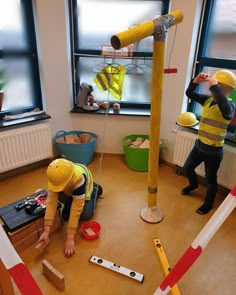 two men in yellow safety vests are working on construction equipment inside a room with windows