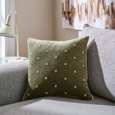 a green pillow sitting on top of a gray couch next to a lamp and window