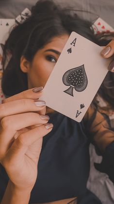 a woman laying on top of a bed holding up a playing card in her hand