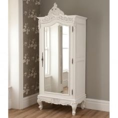 an ornate white armoire stands against a wall in a room with floral wallpaper