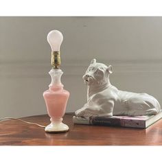 a white dog figurine sitting next to a pink lamp on a wooden table