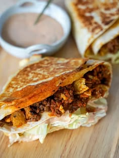 a close up of a sandwich on a cutting board with dipping sauce in the background