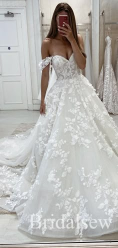 a woman taking a selfie in a wedding dress with flowers on the skirt and off the shoulder