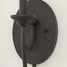 a black wall mounted light on the side of a white wall with a hook in it