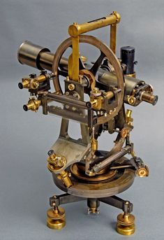 an old fashioned machine with brass parts on it's legs and wheels, sitting on a gray surface