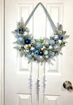 a christmas wreath hanging on the front door with blue and silver balls, pine cones, evergreen leaves and bells