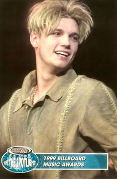 a young man with blonde hair wearing a brown shirt and smiling at the camera while standing in front of a black background