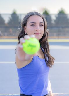 a woman is holding a tennis ball and pointing it at the camera with her right hand