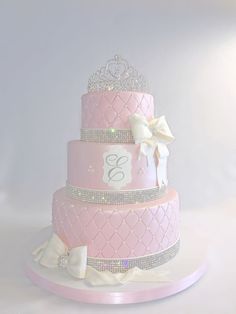 a three tiered pink cake with white bows and tiara on the top layer