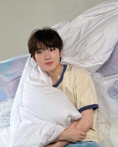 a young man sitting on top of a bed covered in white sheets