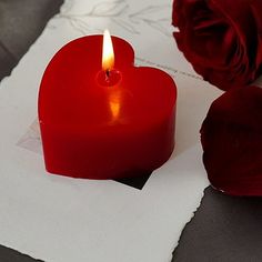 a red heart shaped candle sitting on top of a piece of paper next to a rose