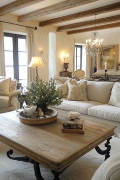 a living room filled with furniture and a chandelier hanging from the ceiling over a wooden coffee table