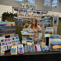 a woman standing in front of a table with art on display at an outdoor market