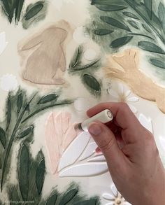 someone is painting leaves on a wall with white paint and green, pink, yellow and brown colors