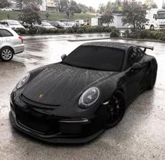 a black sports car parked in a parking lot next to other cars on a rainy day