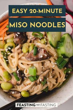 a white bowl filled with noodles, carrots and cucumbers next to chopsticks