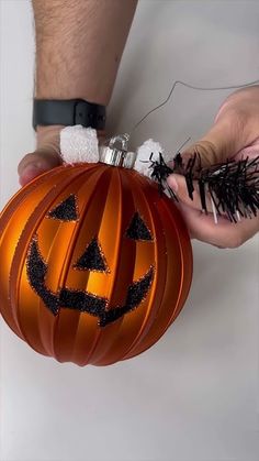 two hands holding an ornament shaped like a jack - o'- lantern