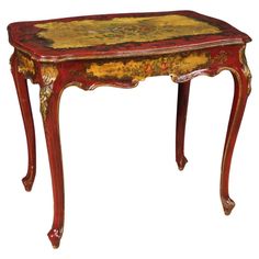 an ornately painted table with red legs and a gold leaf design on the top