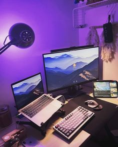 a desk with two computer monitors and a laptop on it, in front of a purple light