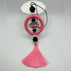 a pink steering wheel and tassel hanging from a hook on a white wall with a black cord