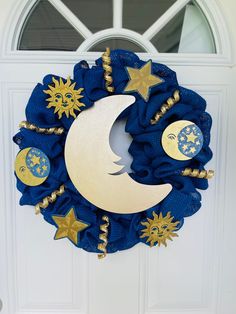 a blue wreath with gold stars and the moon on it is hanging in front of a white door