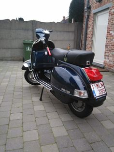 a black motorcycle parked on top of a brick road next to a building and trash can