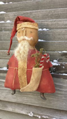 a santa clause doll hanging on the side of a building with snow around him and holding a potted plant