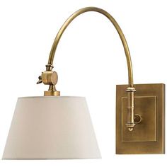 a wall light with a white shade on the side and a gold finish to it