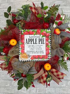 an apple pie wreath with apples and greenery on the front, hanging on a brick wall