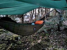 a hammock hanging in the woods with an orange seat on it's side