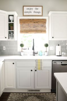 a kitchen with white cabinets and gray subway tile backsplash, window above the sink