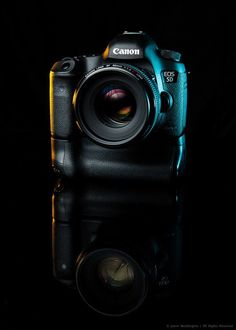 a digital camera sitting on top of a black table next to a light reflecting in the water