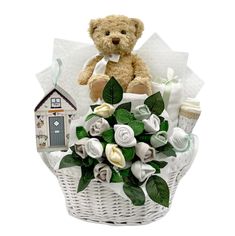 a teddy bear sitting on top of a white basket filled with flowers and baby items