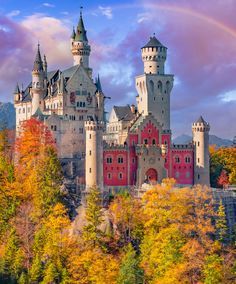 a large castle with two towers surrounded by trees and rainbow in the sky behind it