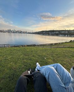 two people are sitting on the grass looking at the water