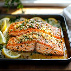 two salmon fillets in a pan with lemons and herbs