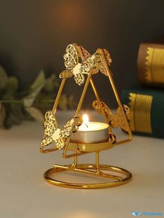 a golden candle holder with a lit candle in the shape of a triangle and two butterflies